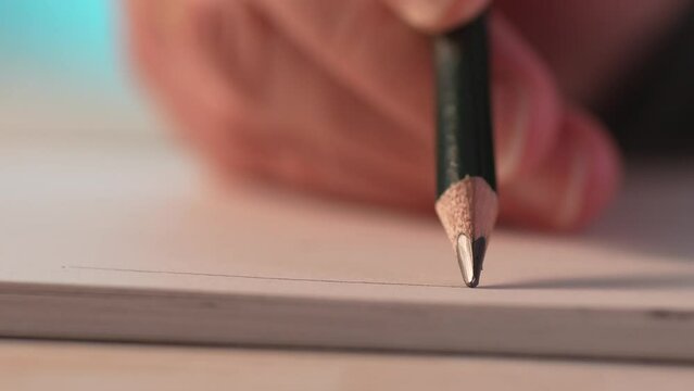 Hand draws lines with a pencil in sketchbook. Close-up, shallow dof.