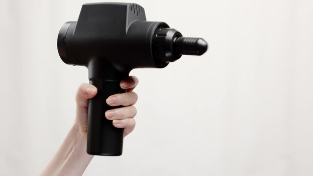 Close-up of woman's hand holding percussion massager with bullet-nozzle and turning it on gray background. Therapy for joint pain relief and physiotherapy