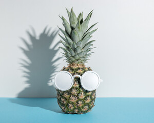 Pineapple with white sunglasses on blue background. Creative minimal summer concept.