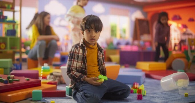 Portrait of an Adorable Multiethnic Asian Boy Looking at Camera and Smiling. Indian Child Playing with Building Blocks in Preschool. Kids Learning and Playing in a Modern Daycare Center