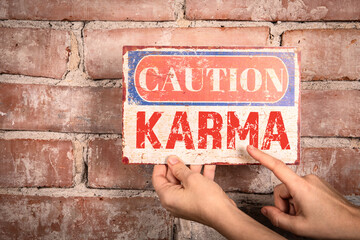 KARMA. Caution sign in a woman's hand on a brick background