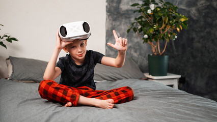A boy is sitting on a soft sofa and testing a VR helmet for games.