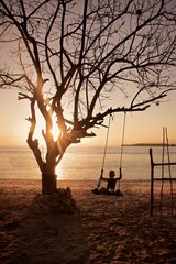 Silhouette of a little boy riding a hanging swing on the beach next to the ocean