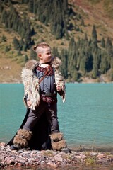 A young boy in the viking cosplay costume standing next to the beautiful alpine lake with Mountains view