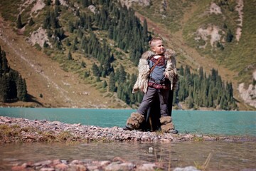 A young boy in the viking cosplay costume standing next to the beautiful alpine lake with Mountains view