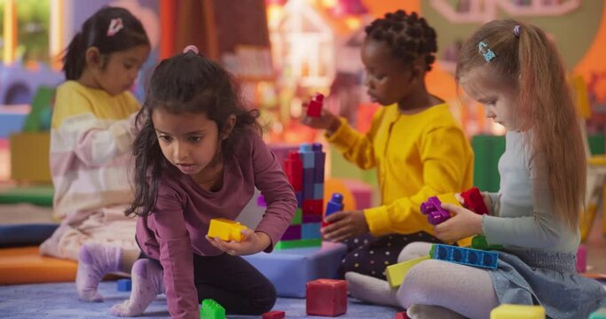 Creative Multiethnic Girlfriends Playing in Kindergarten. African, Indian, Asian and Caucasian Girls Constructing a House Out of Colorful Building Blocks. Children Having Fun in Modern Daycare Center
