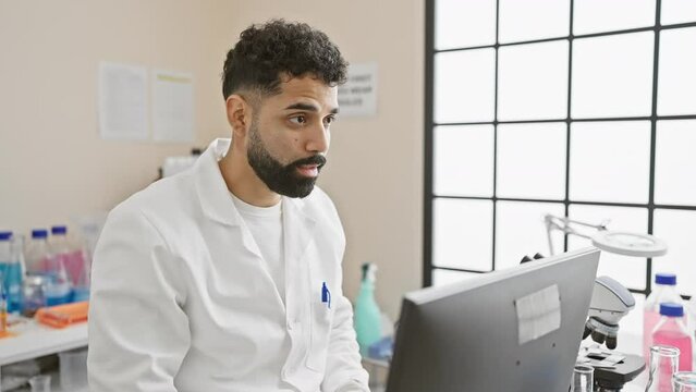 A focused man in a lab coat examining data on a computer monitor in a medical laboratory setting