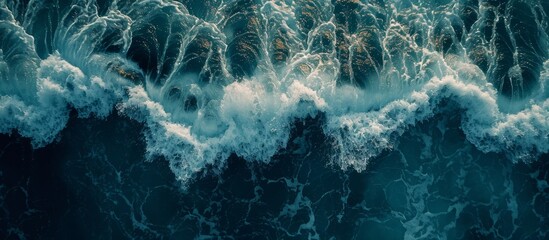 Aerial view of electric blue water with wind waves crashing on the shore creating a captivating pattern. The landscape is dark with cumulus clouds in the sky - obrazy, fototapety, plakaty