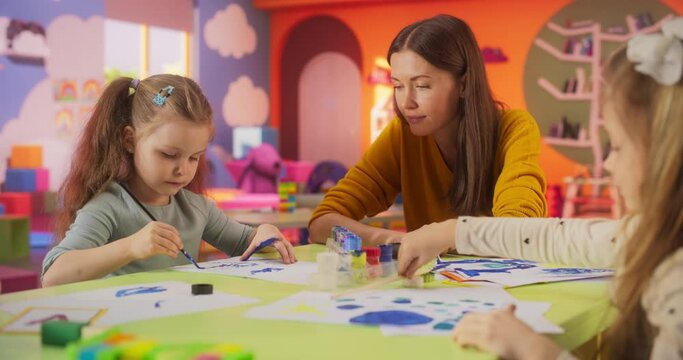 Portrait of Two Adorable Girls Using Watercolor to Create Colorful Paintings on Paper. Cheerful Female Teacher Spending Productive Time in Preschool, Teaching Kids to Paint in Art Class