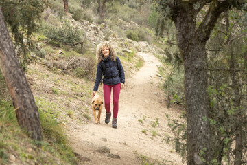 Obraz premium Curly and blonde hair, mountaineer woman and her dog walking through the mountains.
