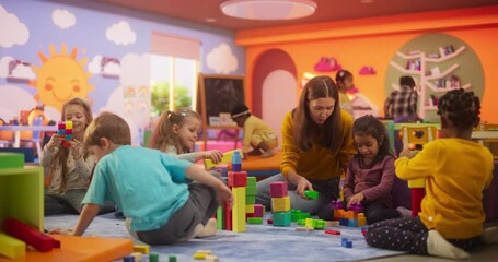 Cheerful Diverse Kids Playing with Colorful Building Block Toys in Kindergarten. Group of Multiethnic Boys and Girls Playing Together with a Female Babysitter in a Modern Daycare Center