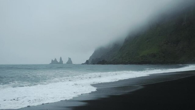 Cinematic black sand beach in Vik, Iceland. Famous tourist travel destination with ocean waves cliff formation view