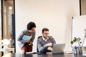 An interracial mentor is standing next to a mentee at the office and giving him advices.