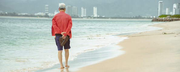Panorama Korean man walking barefoot along white sandy beach shoreline with downtown Nha Trang...