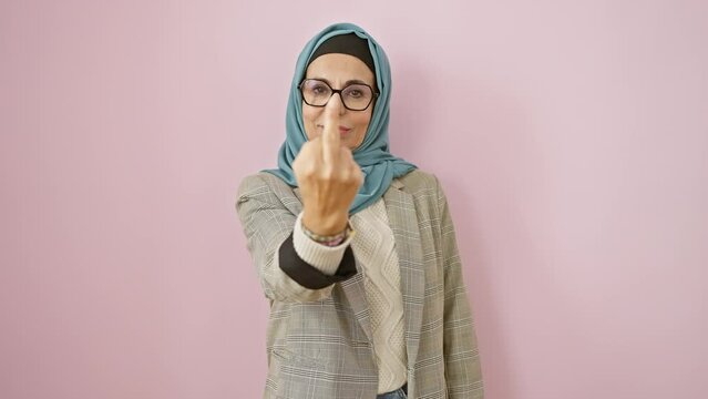Rude show-off! impolite middle age hispanic woman in hijab showing 'fuck you' gesture, an expression of crazy attitude over pink isolated background