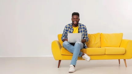 Fotobehang Happy young afro american man sitting in a yellow sofa and using a laptop on a white background. Networking, training, freelancing, remote work. © Irina Sharnina
