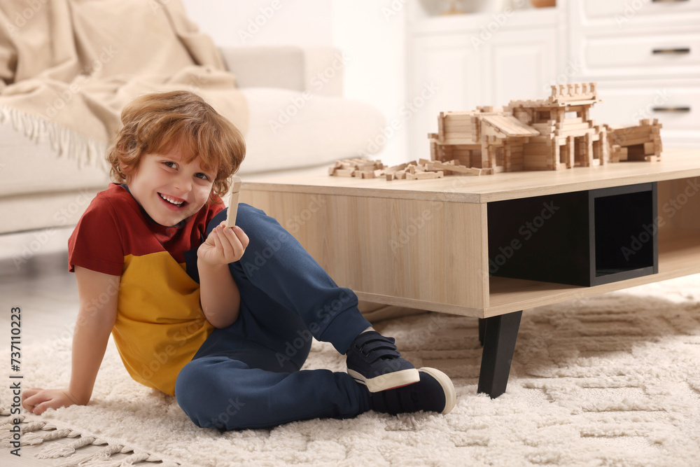 Wall mural Cute little boy playing with wooden construction set on carpet at home. Child's toy