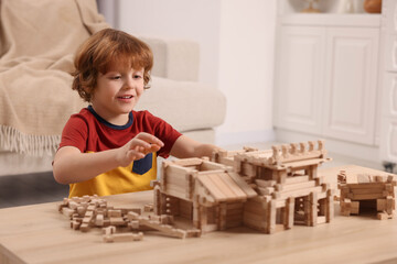 Cute little boy playing with wooden construction set at table in room. Child's toy