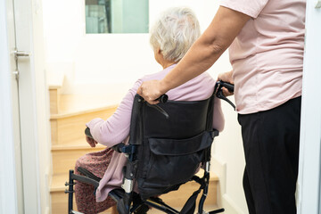 Fototapeta na wymiar Caregiver help asian or elderly old woman sitting wheelchair support up the stairs in home.