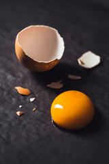 Broken egg with egg yolk on black textured background