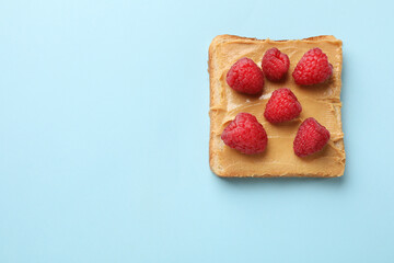 Tasty peanut butter sandwich with fresh raspberries on light blue background, top view. Space for text