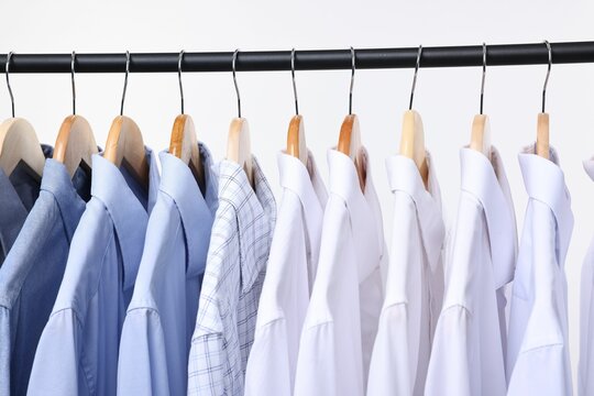 Dry-cleaning service. Many different clothes hanging on rack against white background, closeup