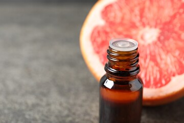 Grapefruit essential oil in bottle and fruit on dark table, closeup. Space for text
