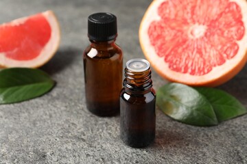 Grapefruit essential oil in bottles, leaves and fruit on dark textured table, closeup
