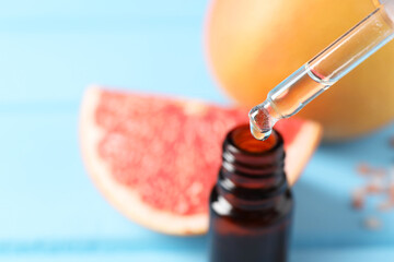 Dripping grapefruit essential oil from pipette into bottle at light blue table, closeup. Space for...