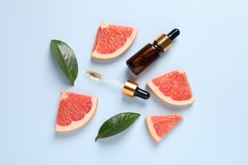 Grapefruit essential oil in bottle, pipette, leaves and cut fruit on light blue table, flat lay