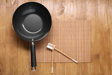Empty iron wok and chopsticks on wooden table, top view. Space for text