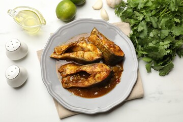 Tasty fish curry and ingredients on white marble table, flat lay. Indian cuisine
