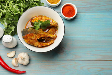 Tasty fish curry and ingredients on light blue wooden table, flat lay. Space for text. Indian cuisine