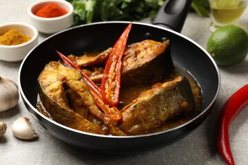 Tasty fish curry in frying pan and ingredients on light grey table, closeup. Indian cuisine