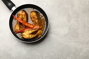 Tasty fish curry in frying pan on light grey table, top view. Space for text. Indian cuisine