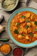 Delicious chicken curry and ingredients on wooden table, flat lay