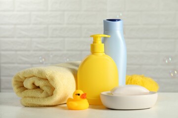 Baby cosmetic products, bath duck, sponge and towel on white table against soap bubbles