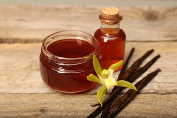 Aromatic vanilla extract, pods and flower on wooden table, closeup