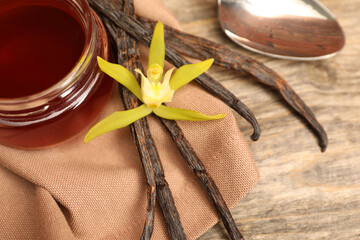 Aromatic vanilla extract, pods and flower on wooden table, closeup