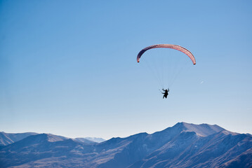 Fototapeta na wymiar Floating effortlessly above the earth, the paraglider enjoys panoramic views of the brown mountain tops.