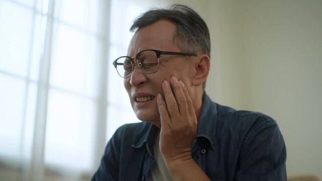 Asian senior man suffering from toothache, tooth problem in elderly man, hurt and pain face, older man holding on cheek with painful, dentist care, unhappy man with inflammation symptom in mouth