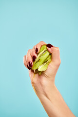 unknown woman with nail polish squeezing green juicy kiwi in her hand on vivid blue background
