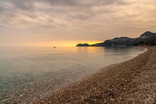 view of the stone pebble beach and clear water at Letojanni on Sicily at sunsest