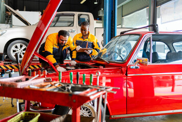 Naklejka premium Diversity mechanic teamwork, an Indian man and an African woman in yellow and blue uniforms. A man inspects the car engine with his woman assistant. Automobile repairing service. Vehicle maintenance.