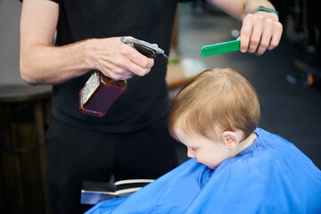 Male hairdresser sprinkling water on client's head. Barber using sprayer bottle with water to get...