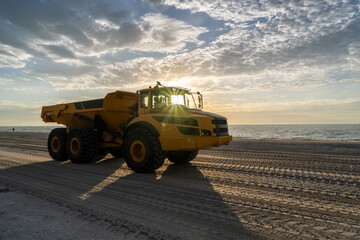 Articulated hauler mining type dump truck, in motion, carrying sand for a restoration project on a beach as the sun rising over the gulf of Mexico, Sanibel Island, Florida