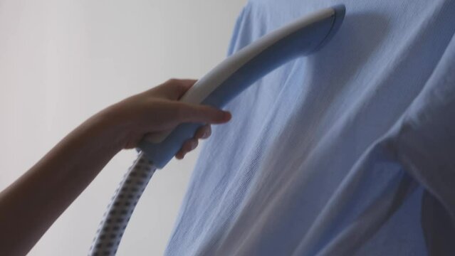A woman steams a shirt with a hand iron and smooths out the creases on it. Housewife chores, tidying up, cleanliness, domestic lifestyle