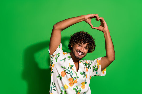 Photo of funky cheerful arabian man wear print shirt rising arms showing heart gesture empty space isolated green color background
