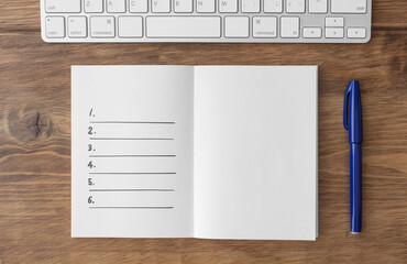 Spread notebook with written lists, keyboard and blue pen on brown wooden desk