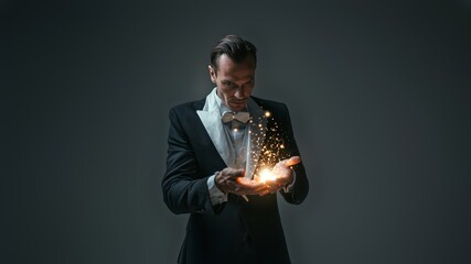 Fototapeta premium Smiling magician in black tuxedo performs a captivating magic trick against a white backdrop.